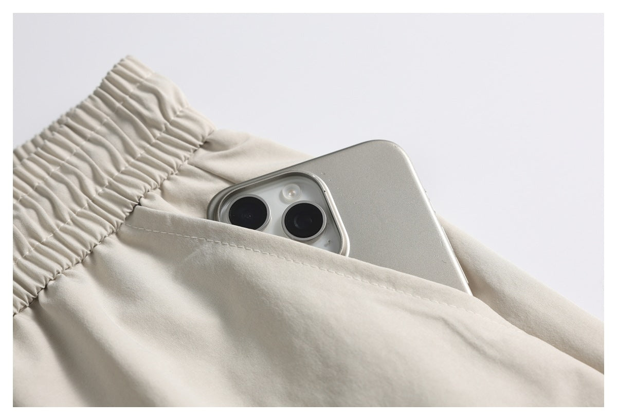 Close-up of a phone tucked into the pocket of light beige shorts beside the gathered waistband.
