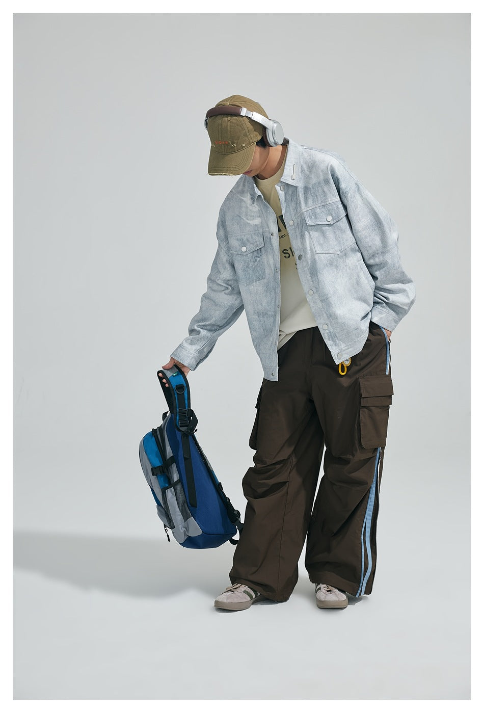 Model wearing a light gray washed jacket with flap chest pockets and dark cargo pants with blue side stripes.