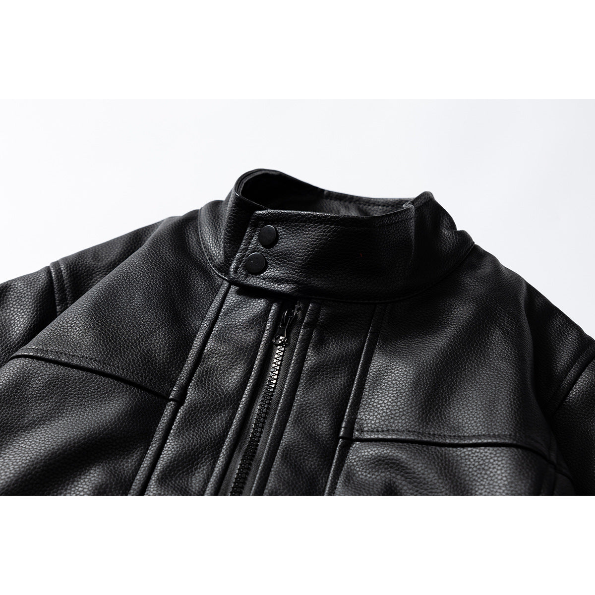Close-up of a black jacket showing its raised snap collar, central zipper, and stitched panels.