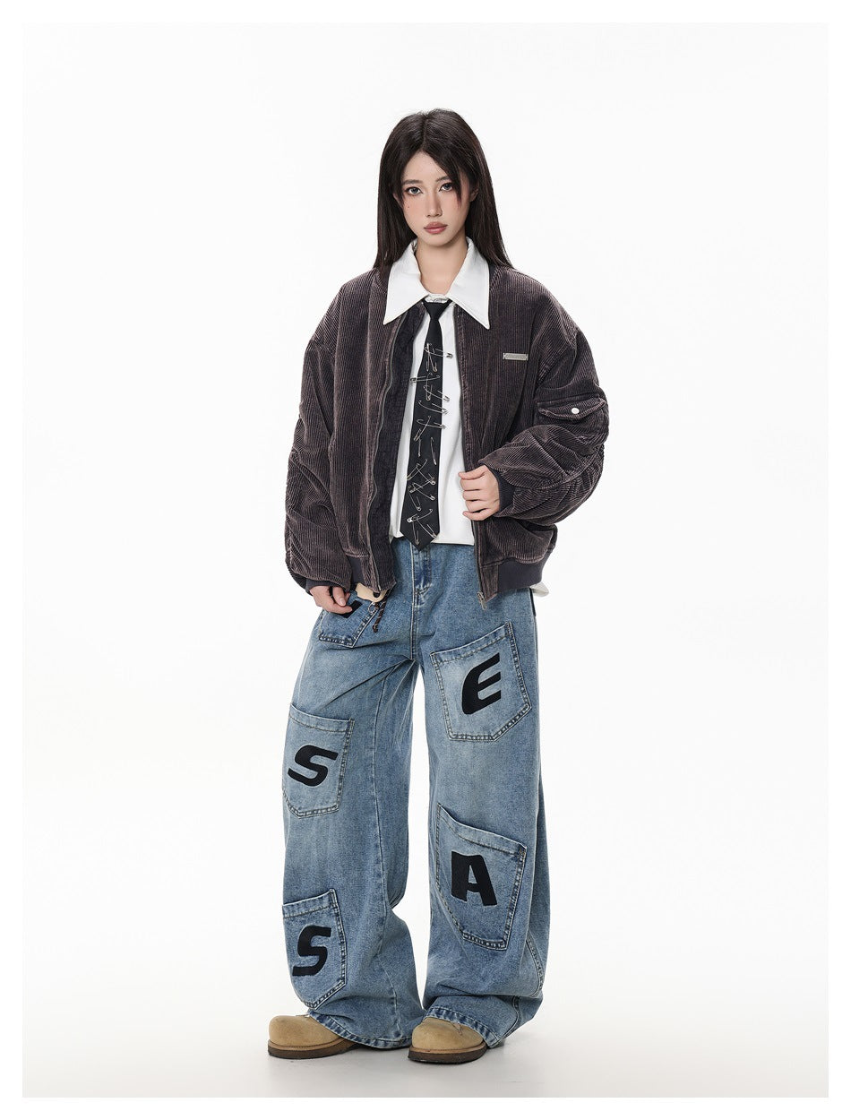 Full-length model wearing a dark brown bomber jacket and oversized blue jeans with large black letter patches.