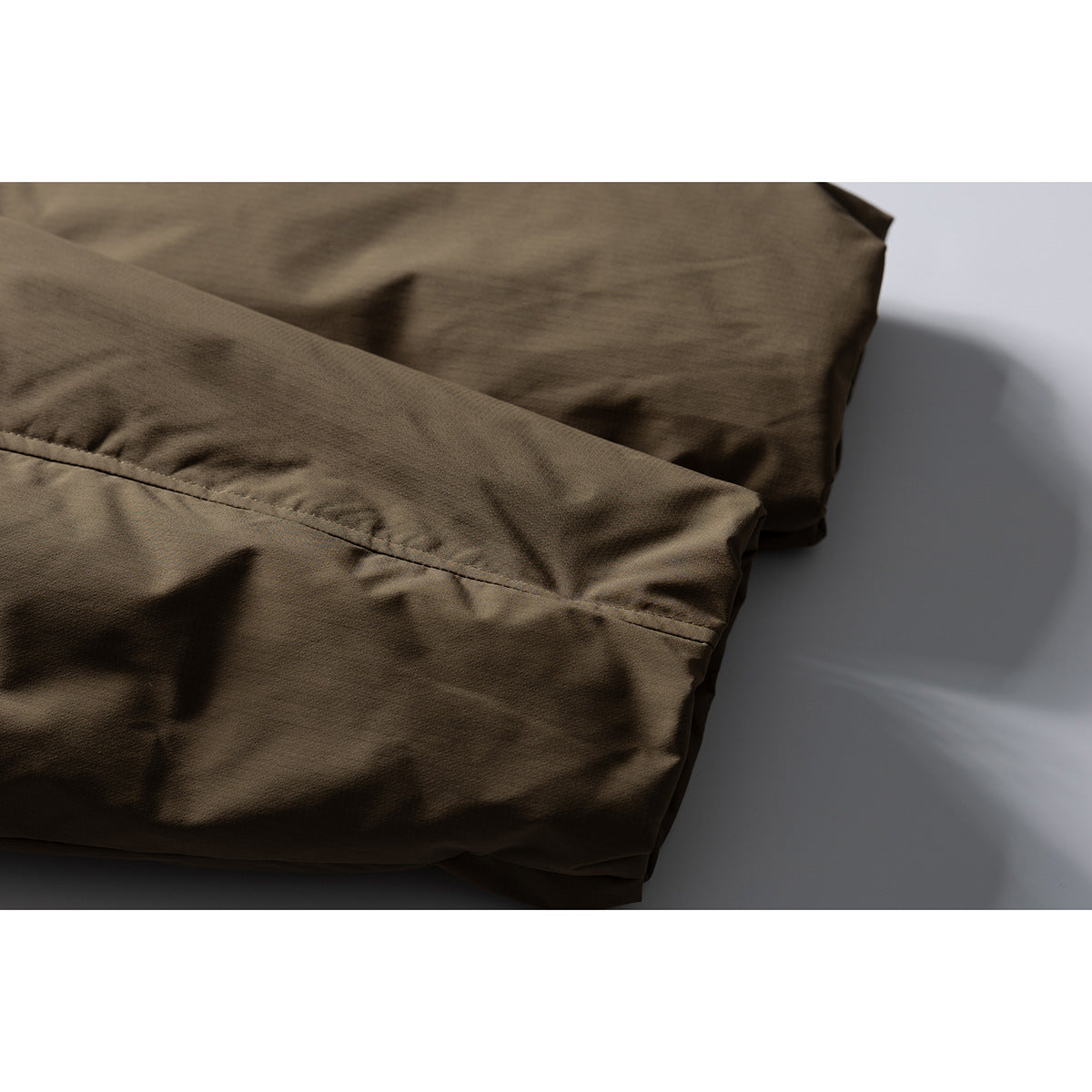 Close-up of the olive-brown jacket’s lower panel and stitched seam.