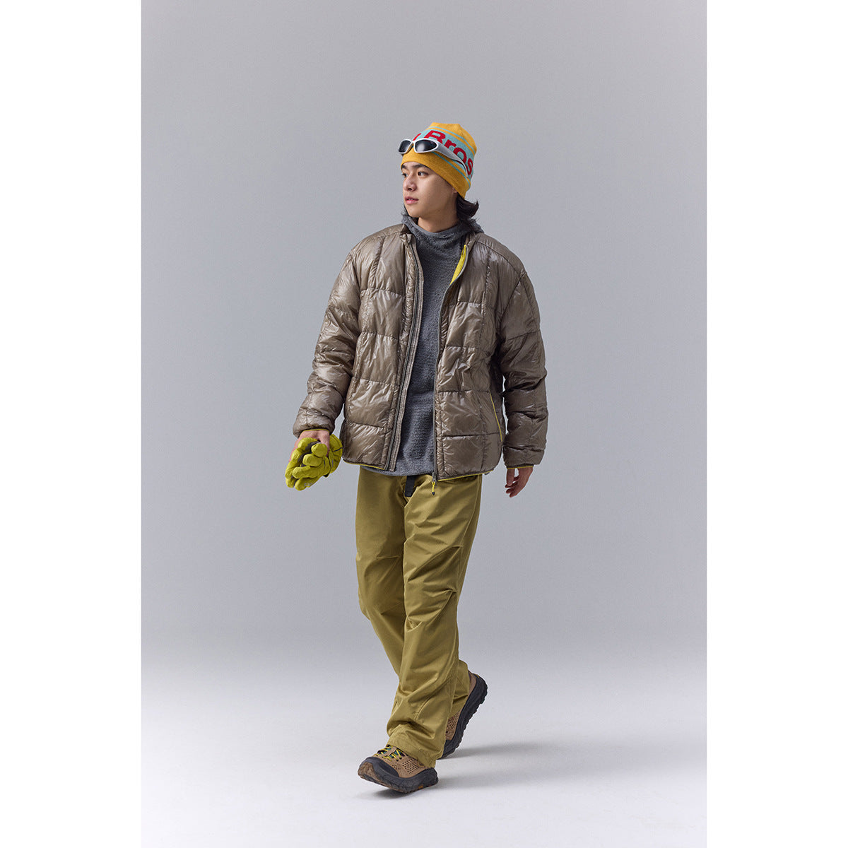 Model wearing a taupe quilted jacket over a gray top, with olive trousers and a yellow beanie.