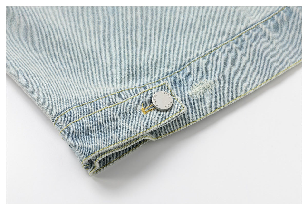 Close-up of light-wash denim with yellow stitching, a metal button, and a small distressed patch.
