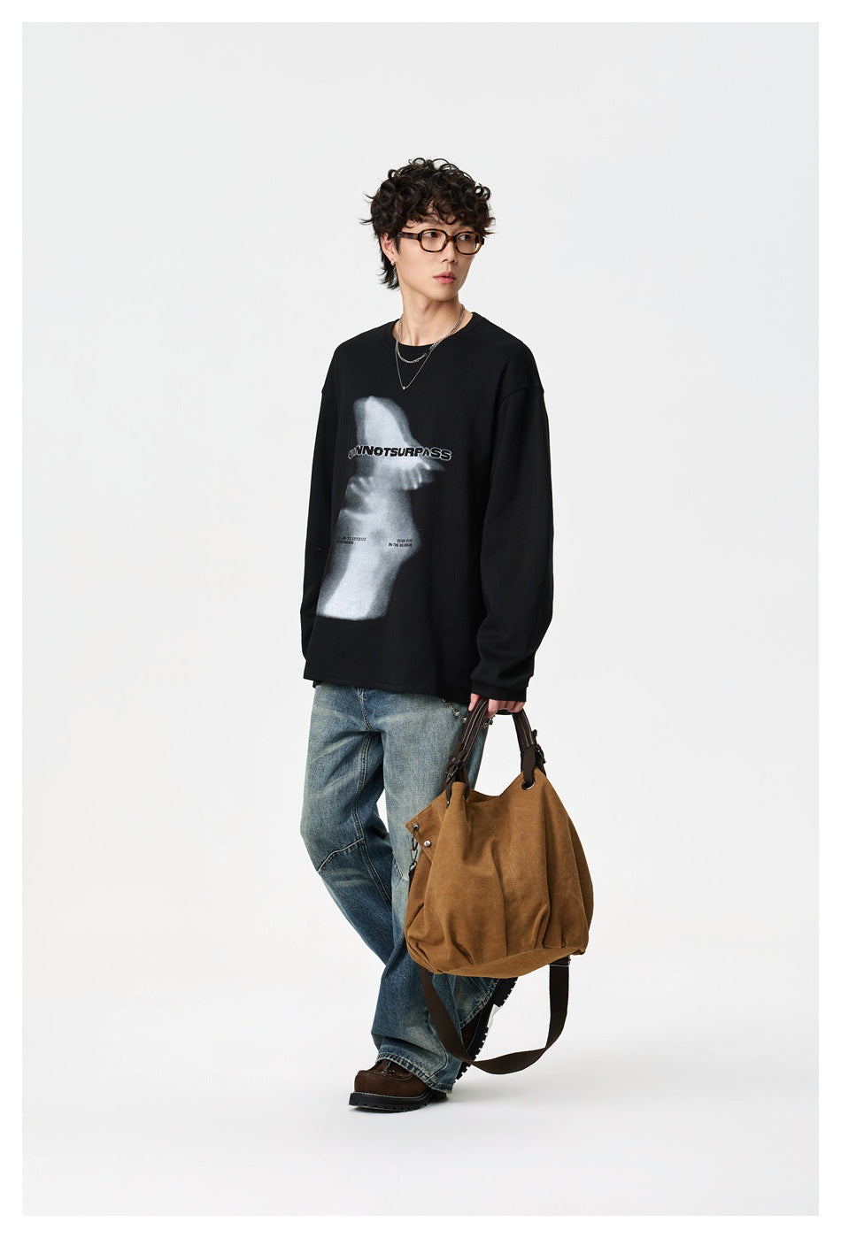 Three-quarter view of a model wearing a black graphic sweatshirt and loose blue jeans with a brown shoulder bag.