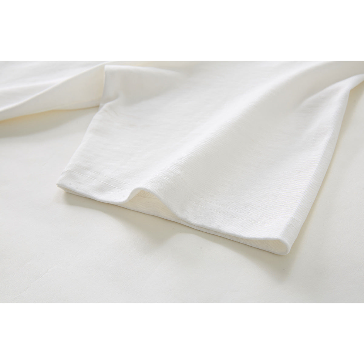 Close-up of the plain off-white T-shirt sleeve and stitched hem.