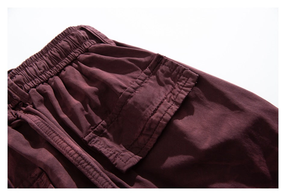 Close-up of a large stitched cargo pocket and elastic waistband on burgundy pants.