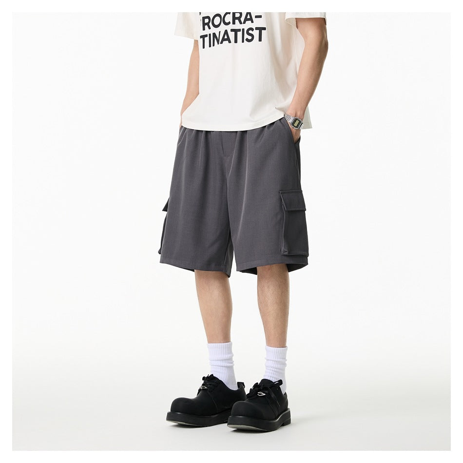 Person wearing gray cargo shorts with a white graphic tee, white socks and black shoes, hand in pocket