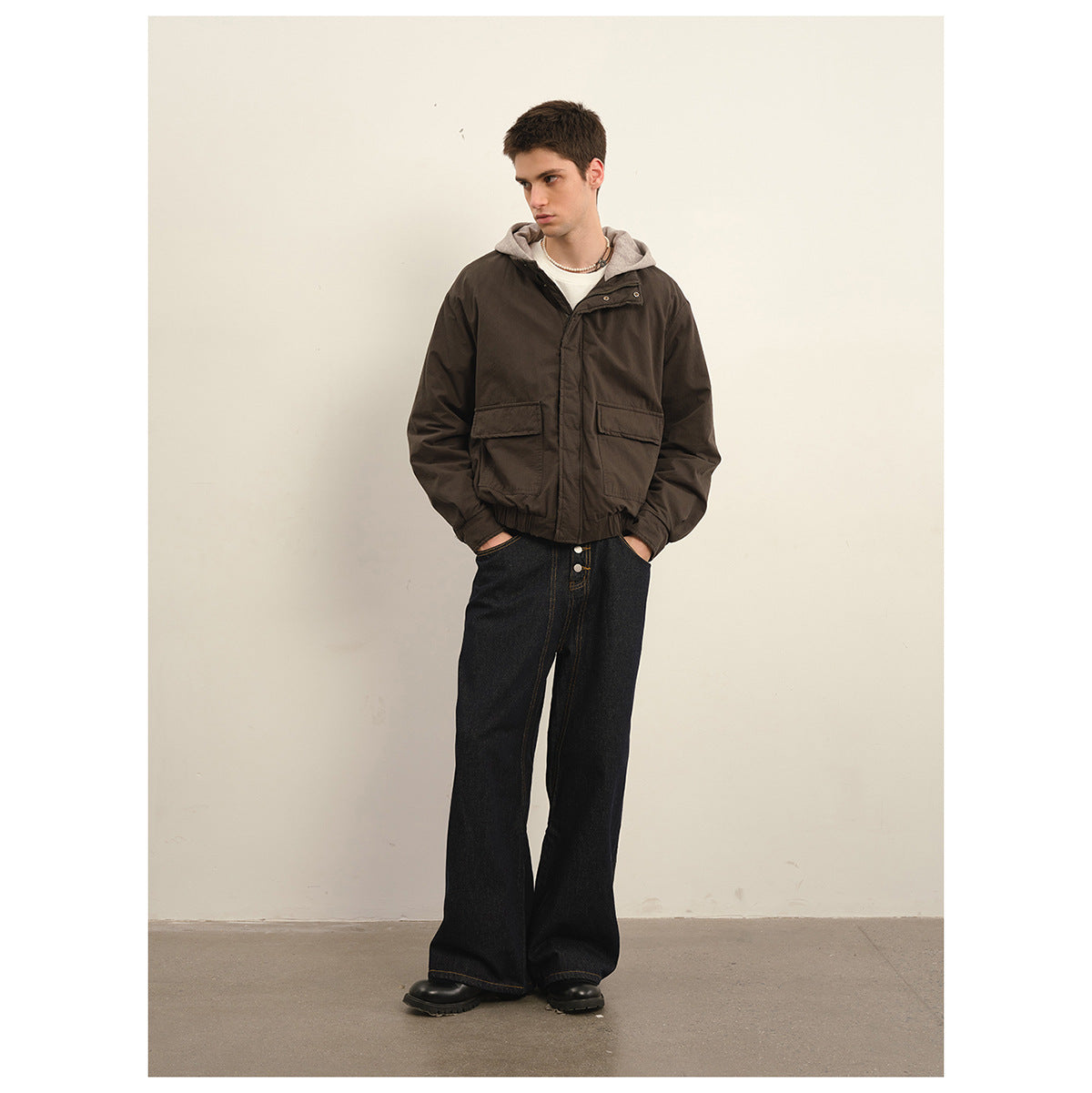 Model wearing a dark brown hooded jacket with flap pockets, wide black jeans, and black boots.