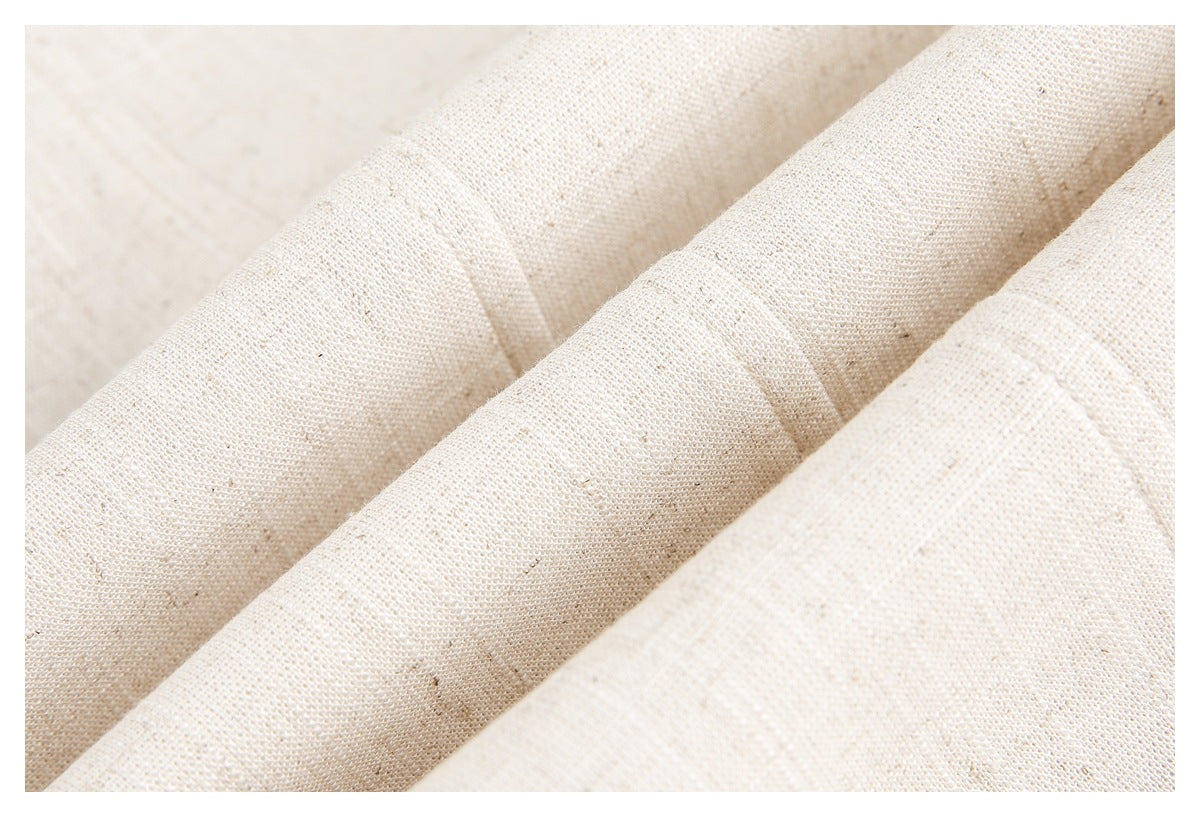 Close-up of off-white woven fabric draped in folds, showing its weave and scattered flecks.
