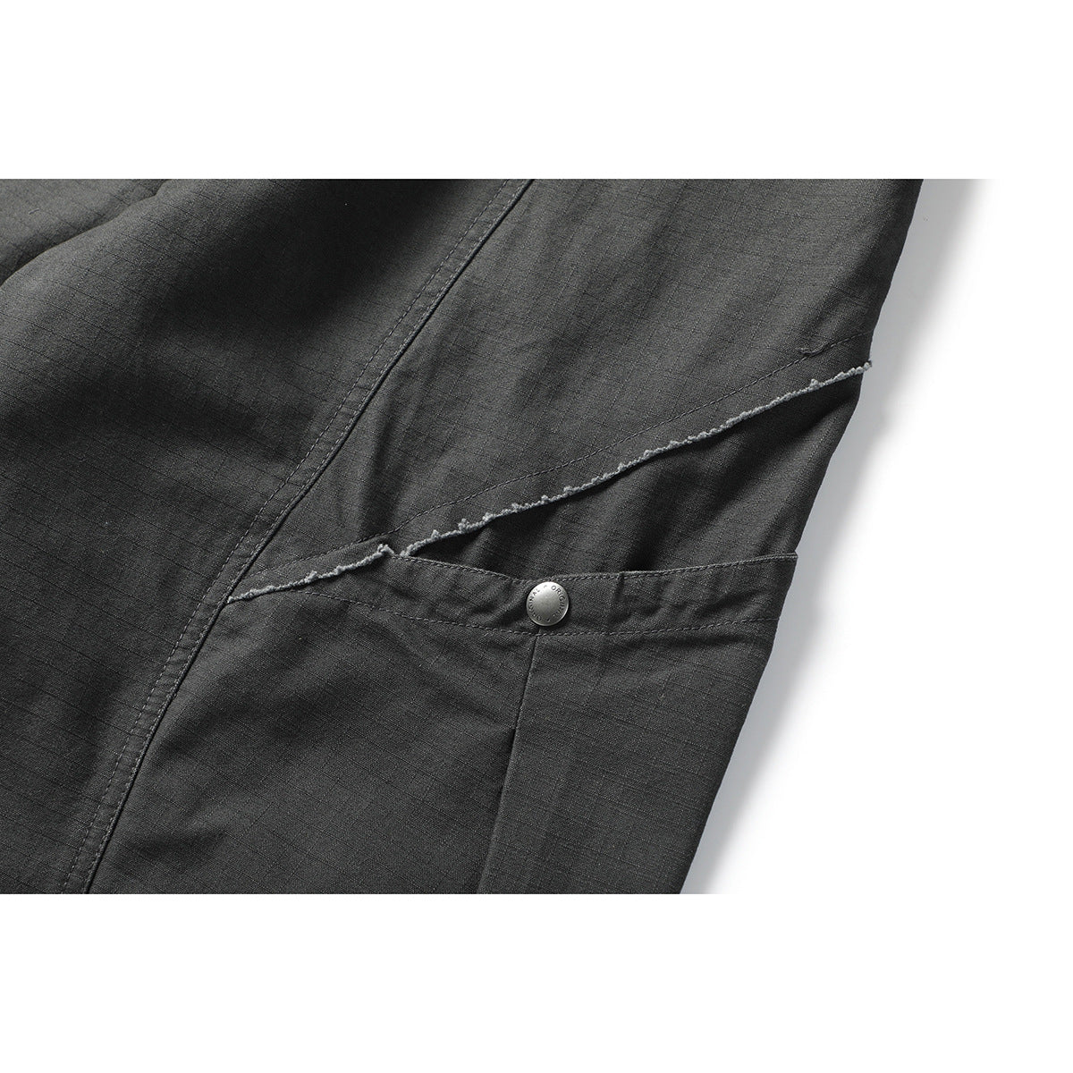 Close-up of charcoal pants showing a diagonal raw-edge seam, a snap-button tab, and visible fabric texture.