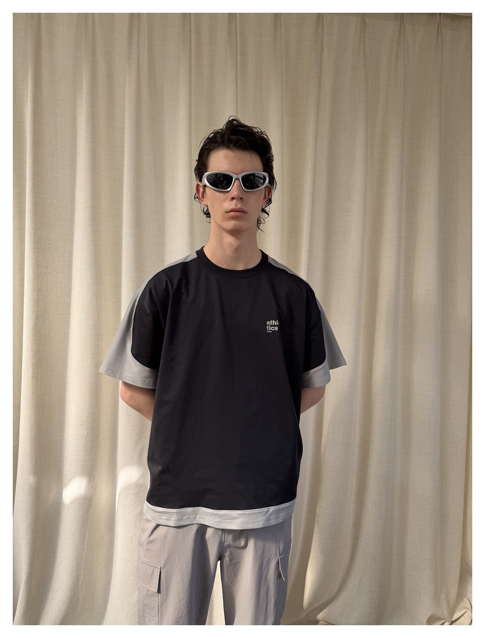 Model wearing a black T-shirt with light gray sleeves and hem, paired with gray cargo pants.