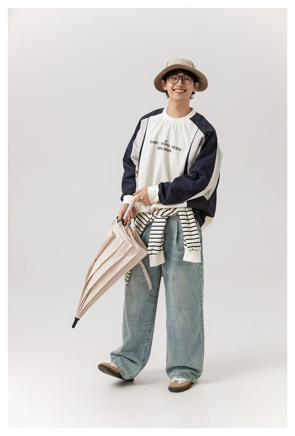Full-length model wearing an ivory and navy pullover, striped shirt tied at the waist, and loose light-wash jeans.