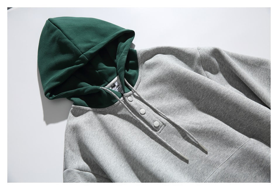 Close view of a gray hoodie with a dark green hood, gray drawstrings, and a three-snap placket.
