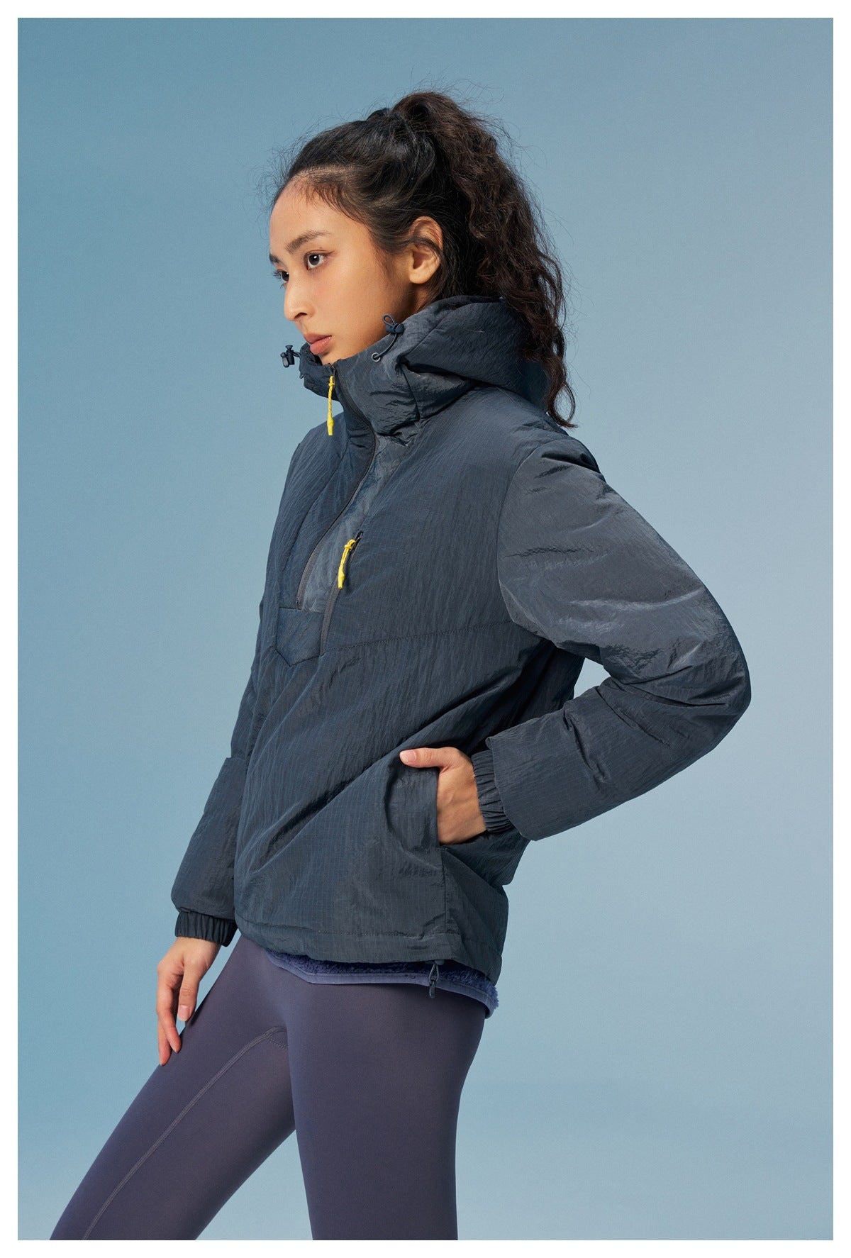 Side view of woman in a dark gray hooded half-zip jacket with a hand in the side pocket