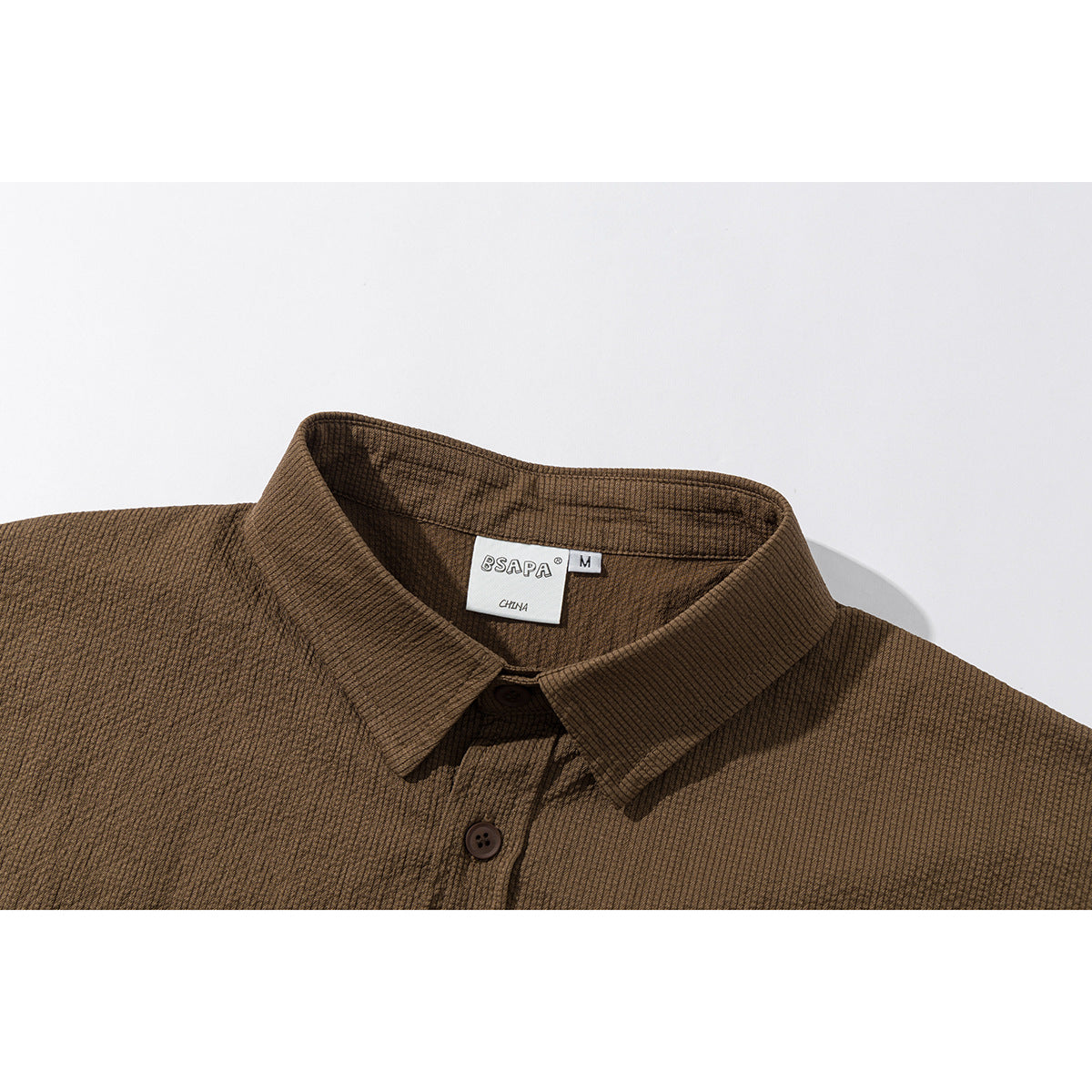 Close-up of a brown finely textured shirt showing its pointed collar, top button and neck label.