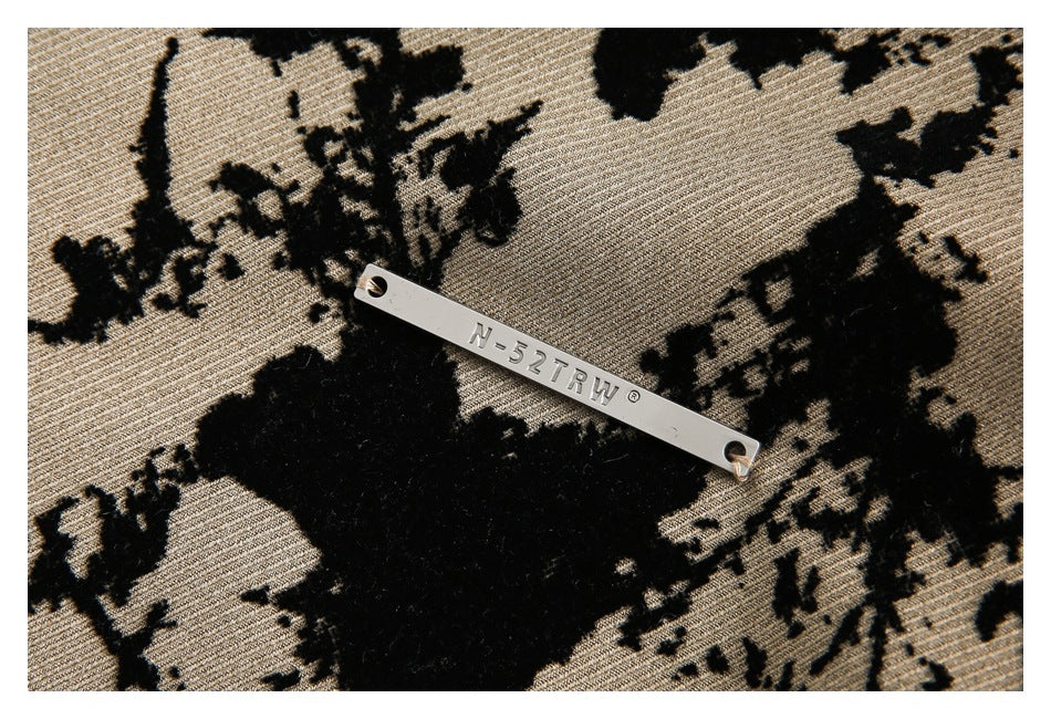 Silver metal N-52TRY plaque attached to tan fabric with a black abstract floral pattern.