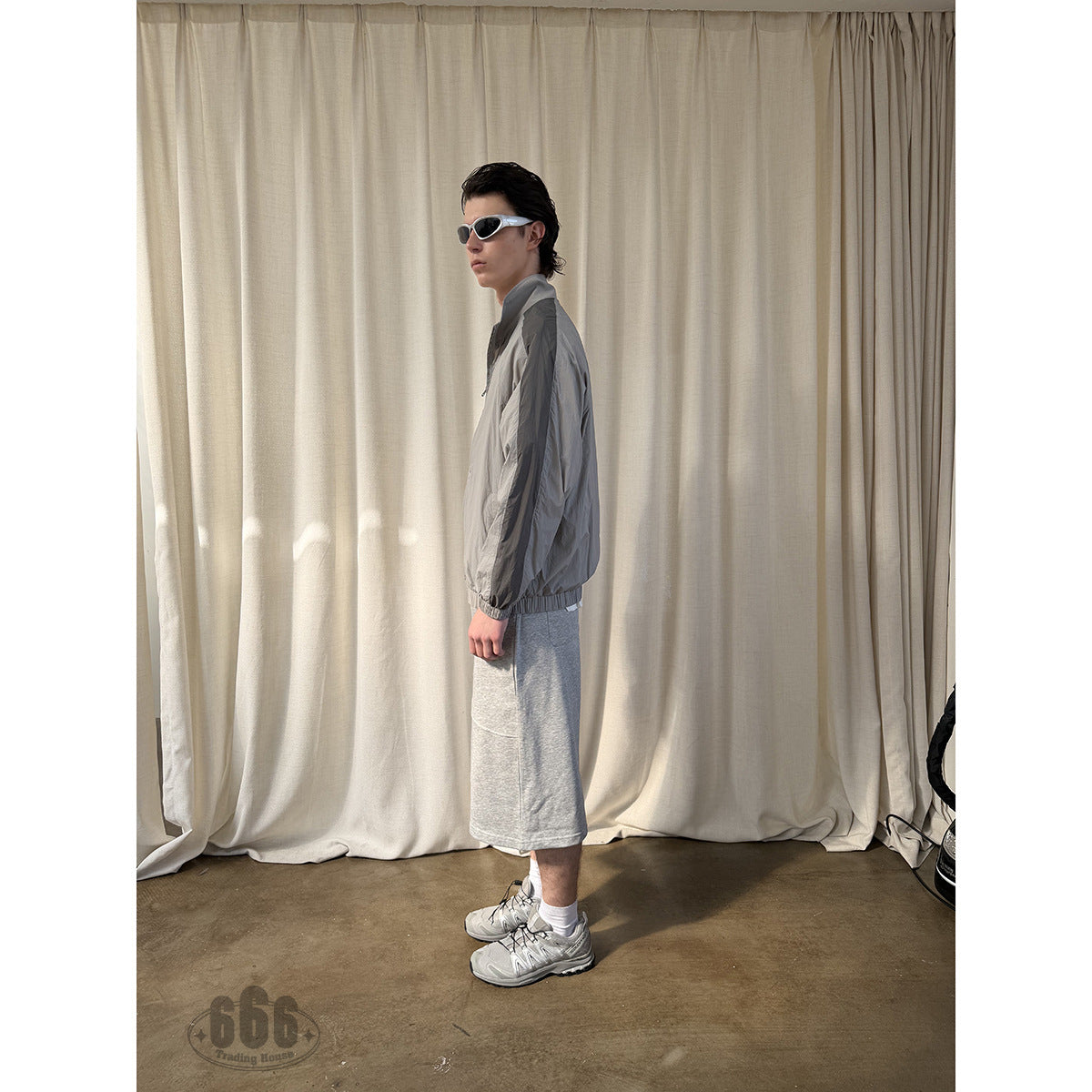 Side view of a model wearing light gray knee-length shorts with a curved pocket.