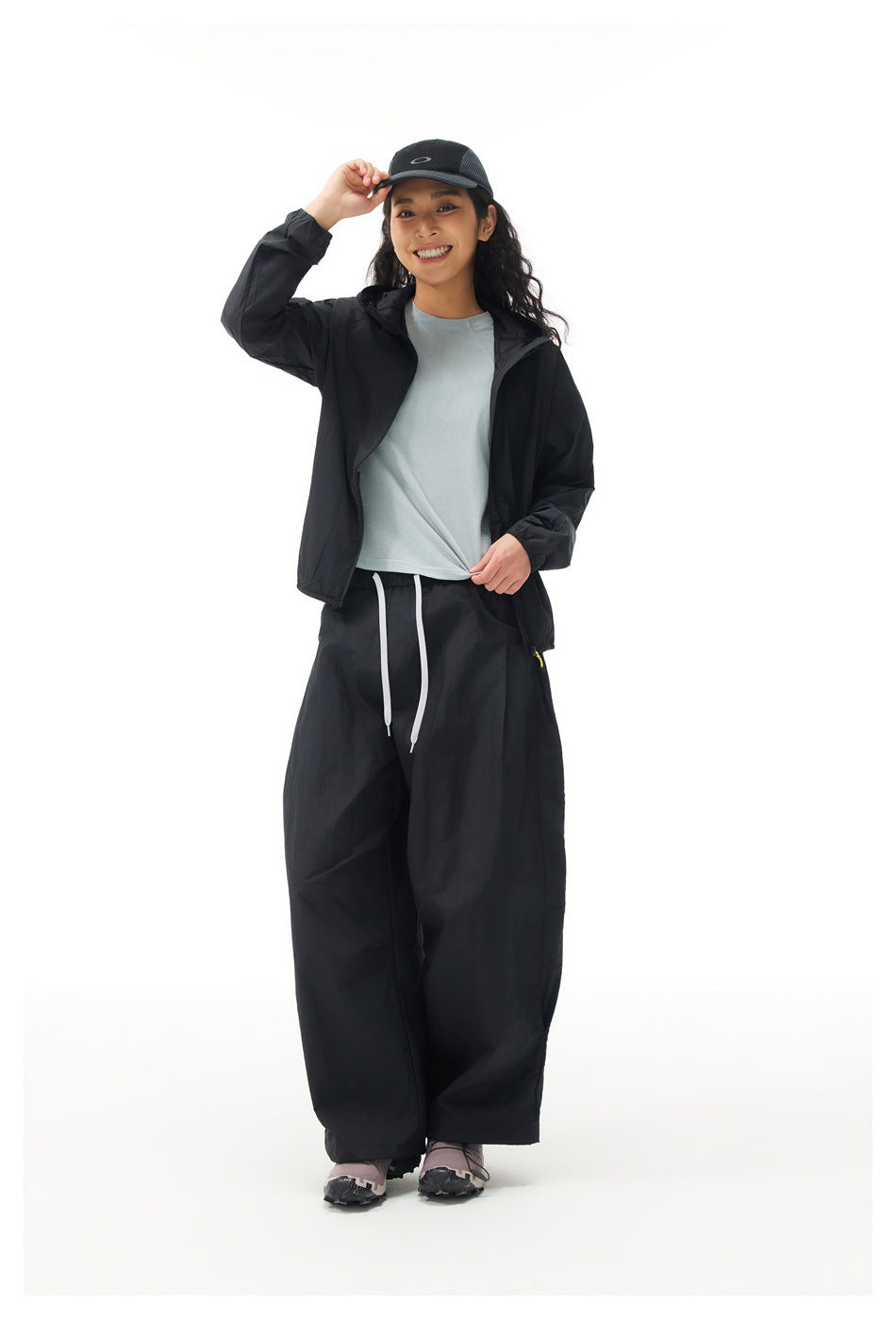 Full-length model wearing an open black jacket over a pale blue shirt with loose black drawstring trousers.