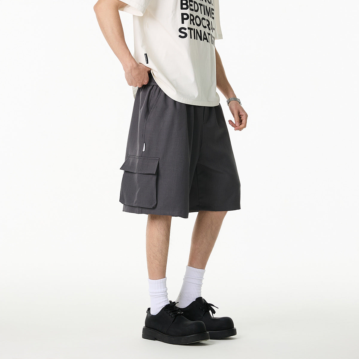 Model wearing loose charcoal-gray cargo shorts with large flap pockets, shown from a front-side angle.