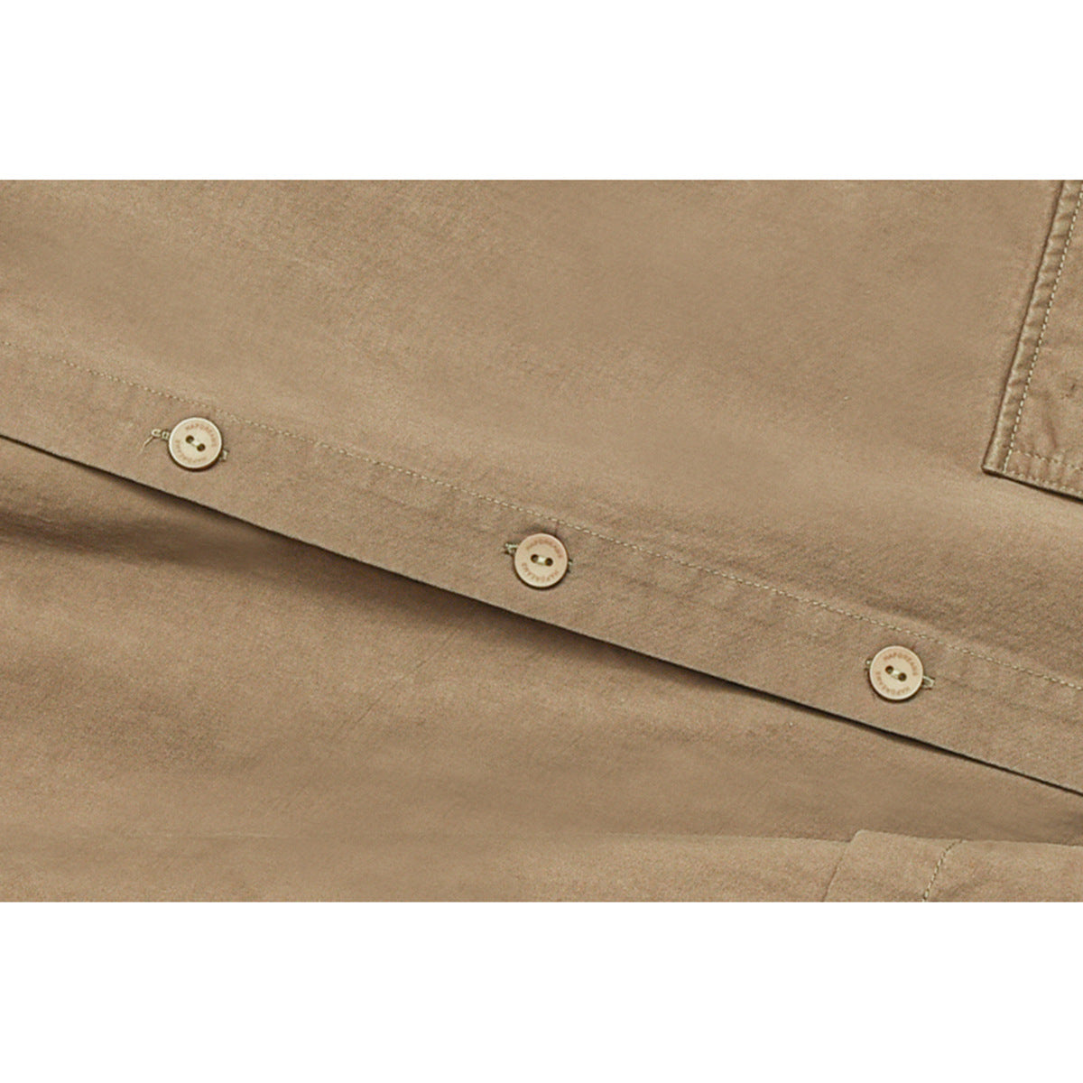 Close-up of a tan shirt's button placket, showing three light buttons and stitching.