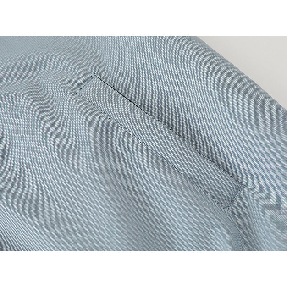 Close-up of a pale blue jacket’s narrow diagonal welt pocket.
