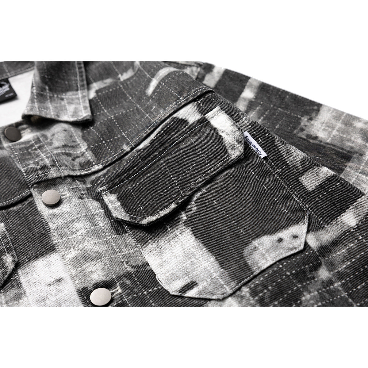 Close-up of a flap chest pocket and snap buttons on a charcoal and gray abstract plaid jacket.