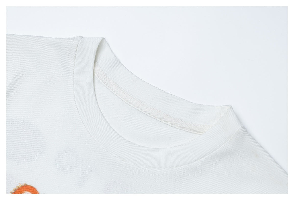 Close-up of a white T-shirt's ribbed crew neckline and shoulder seam, with a small orange print edge visible.