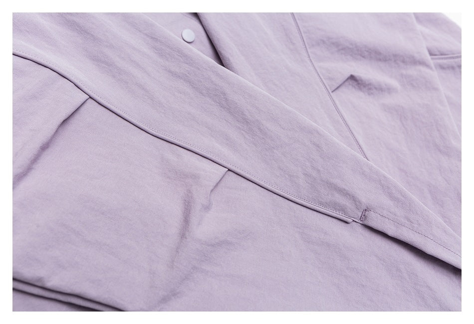 Close-up of a pale lavender garment with a diagonal overlapping panel, covered button, and stitched pocket detail.