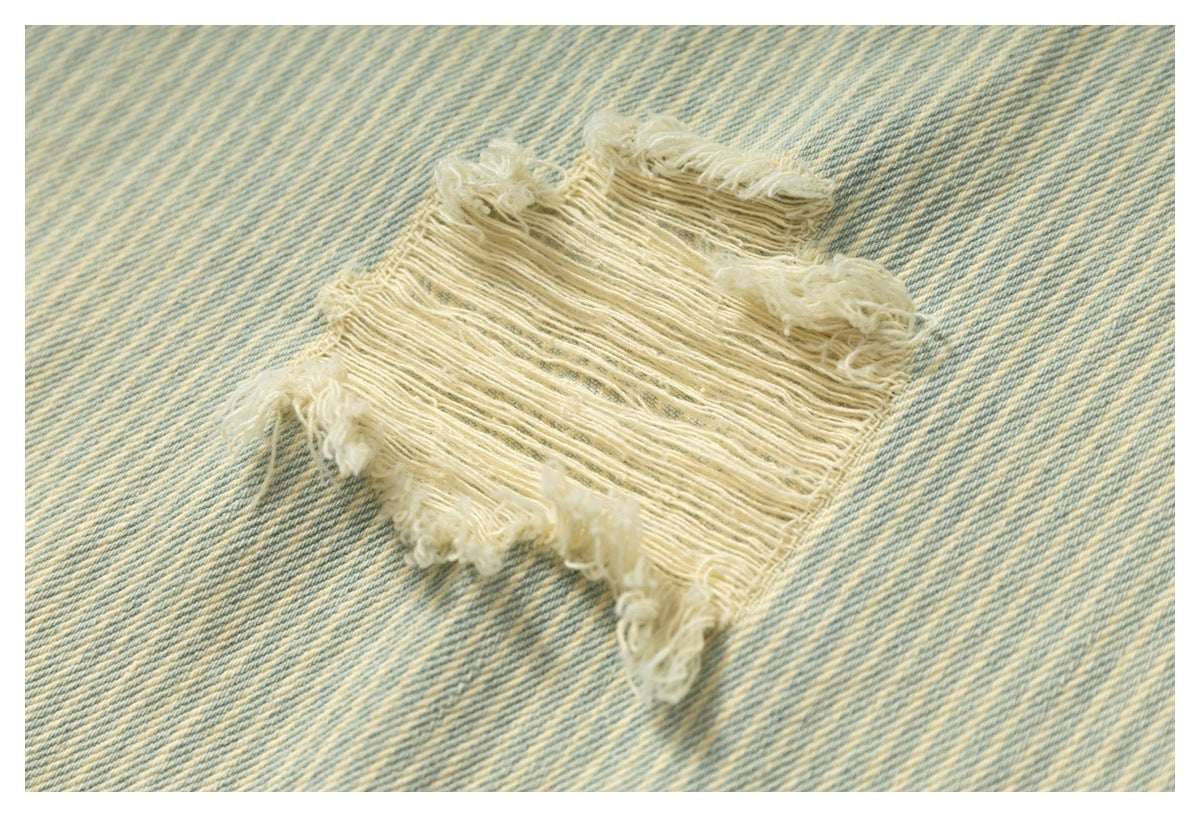 Close-up of a frayed distressed patch on pale blue and cream striped denim.