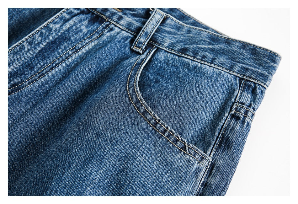 Close-up of blue washed jeans showing a curved front pocket, belt loop, and contrast stitching.