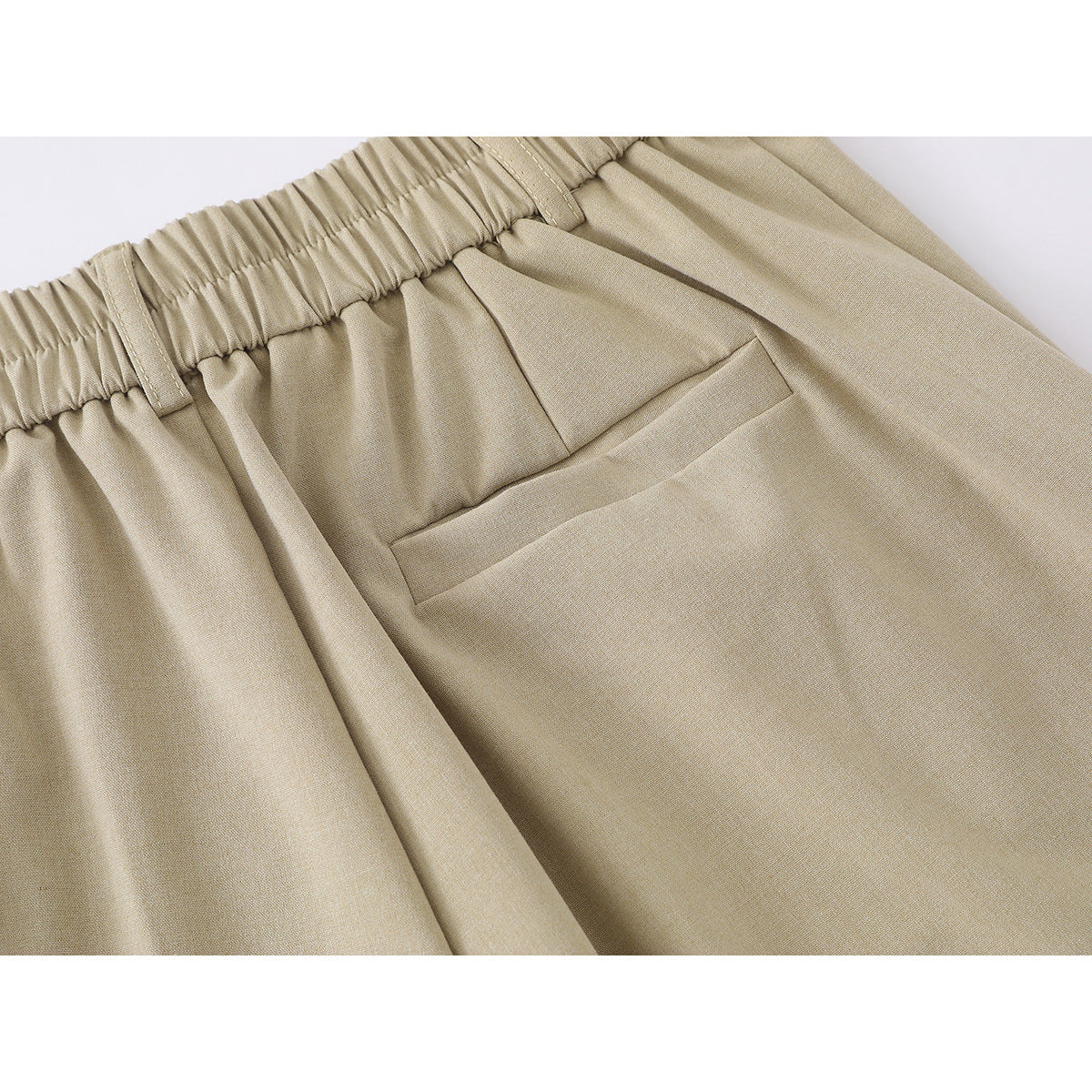 Close-up of beige shorts showing the gathered elastic back waistband and a welt pocket.