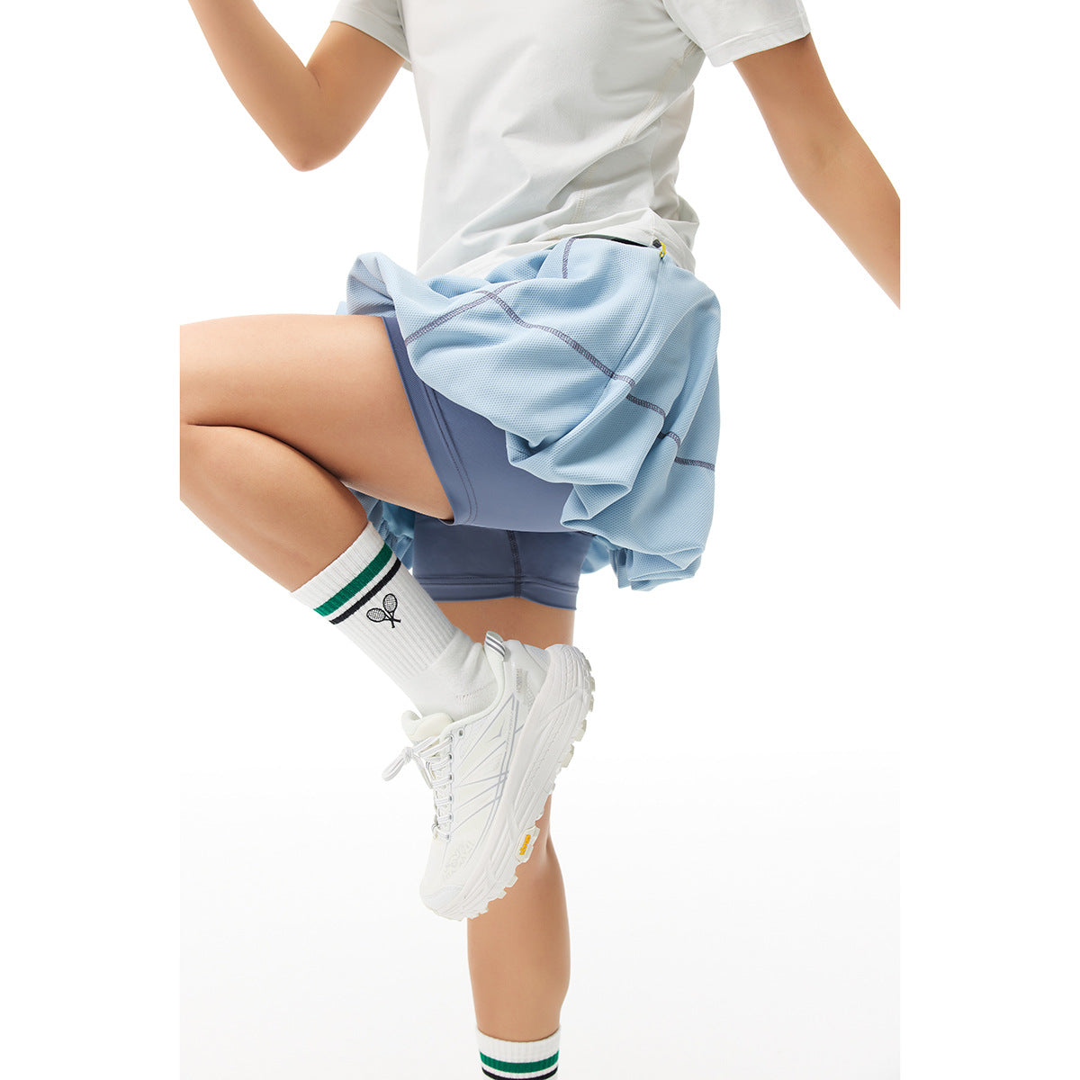 Close view of a model in a light blue bubble tennis skirt with blue built-in shorts, shown in a bent pose.