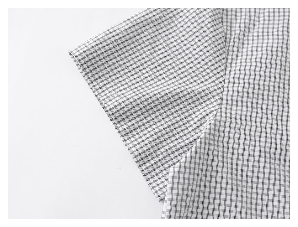 Close-up of a sleeve folded across the body of a white shirt with a fine black grid check.