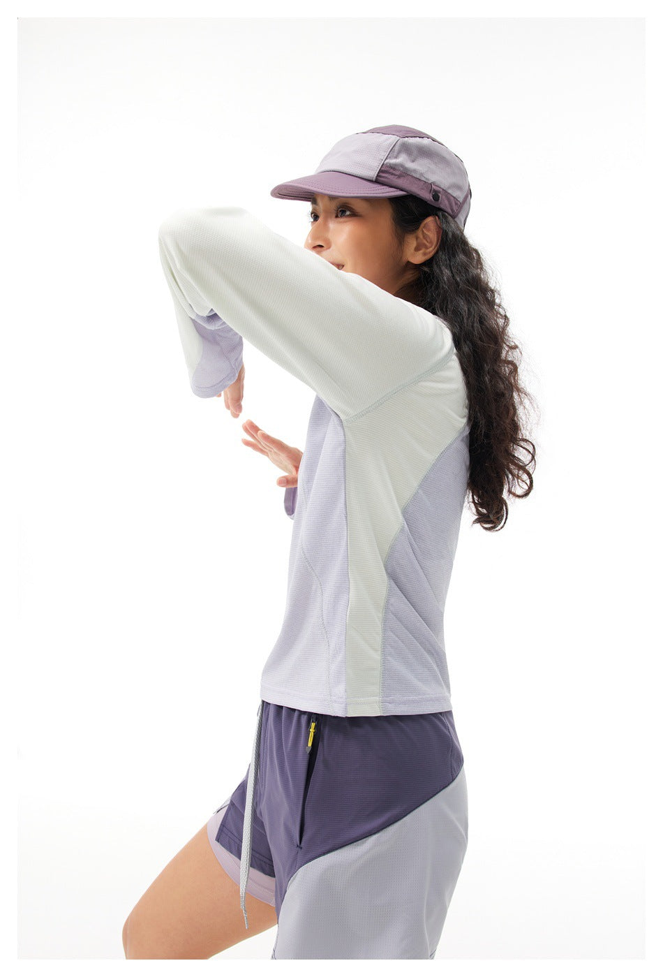 Model wearing a pale mint and lavender color-block long-sleeve top with matching lavender shorts and a cap.