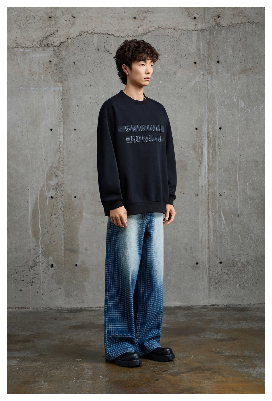 Model wearing a black crewneck sweatshirt with raised chest lettering, shown from a slight angle.