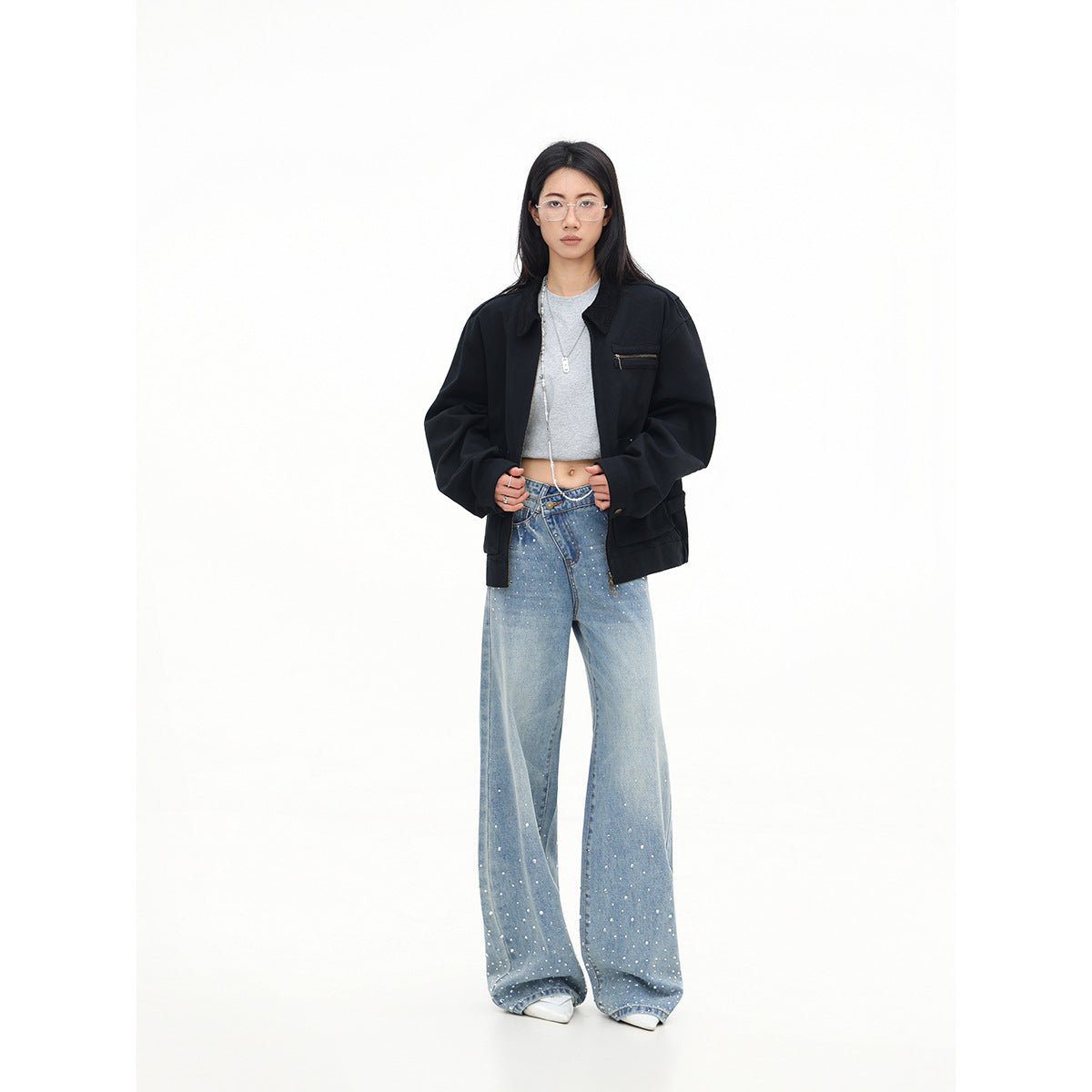 Model wears an open black oversized jacket with a zip chest pocket over a gray crop top and embellished wide-leg jeans.