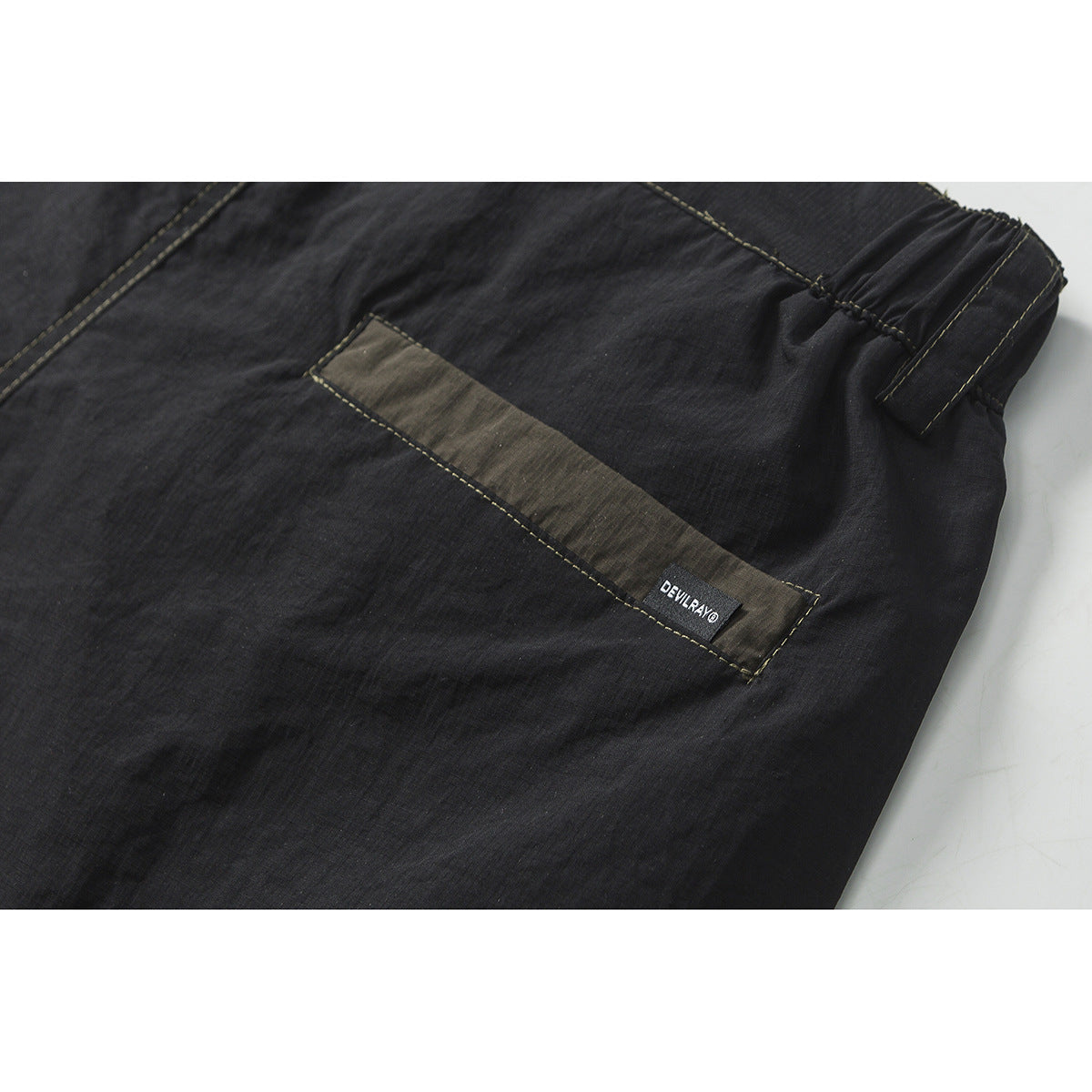 Close-up of charcoal shorts with an olive-toned pocket panel, elastic waistband, and small sewn-in label.