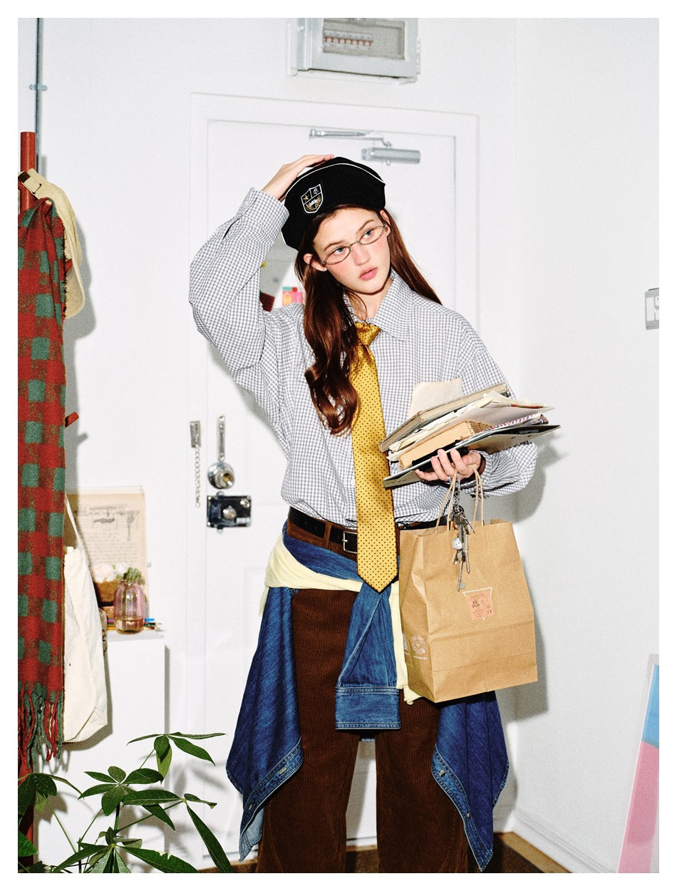 Model wearing a gray-and-white checked shirt and yellow tie, holding books and a paper bag.