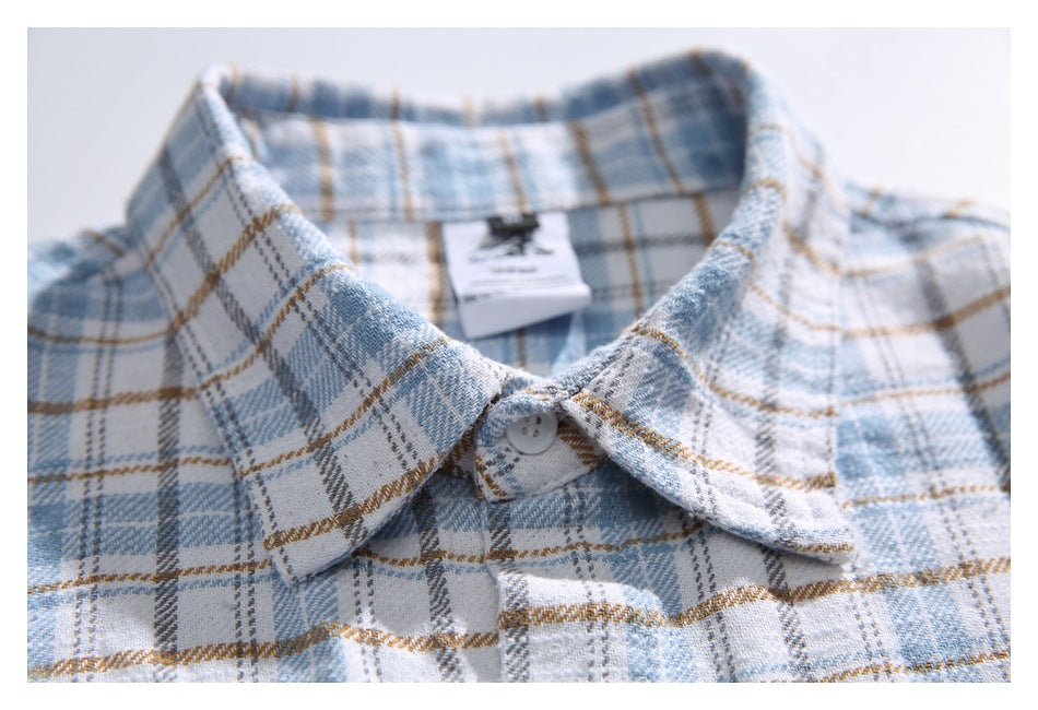 Close-up of a pointed collar and top button on a light blue, gray, white, and tan plaid shirt, with an inner neck label.