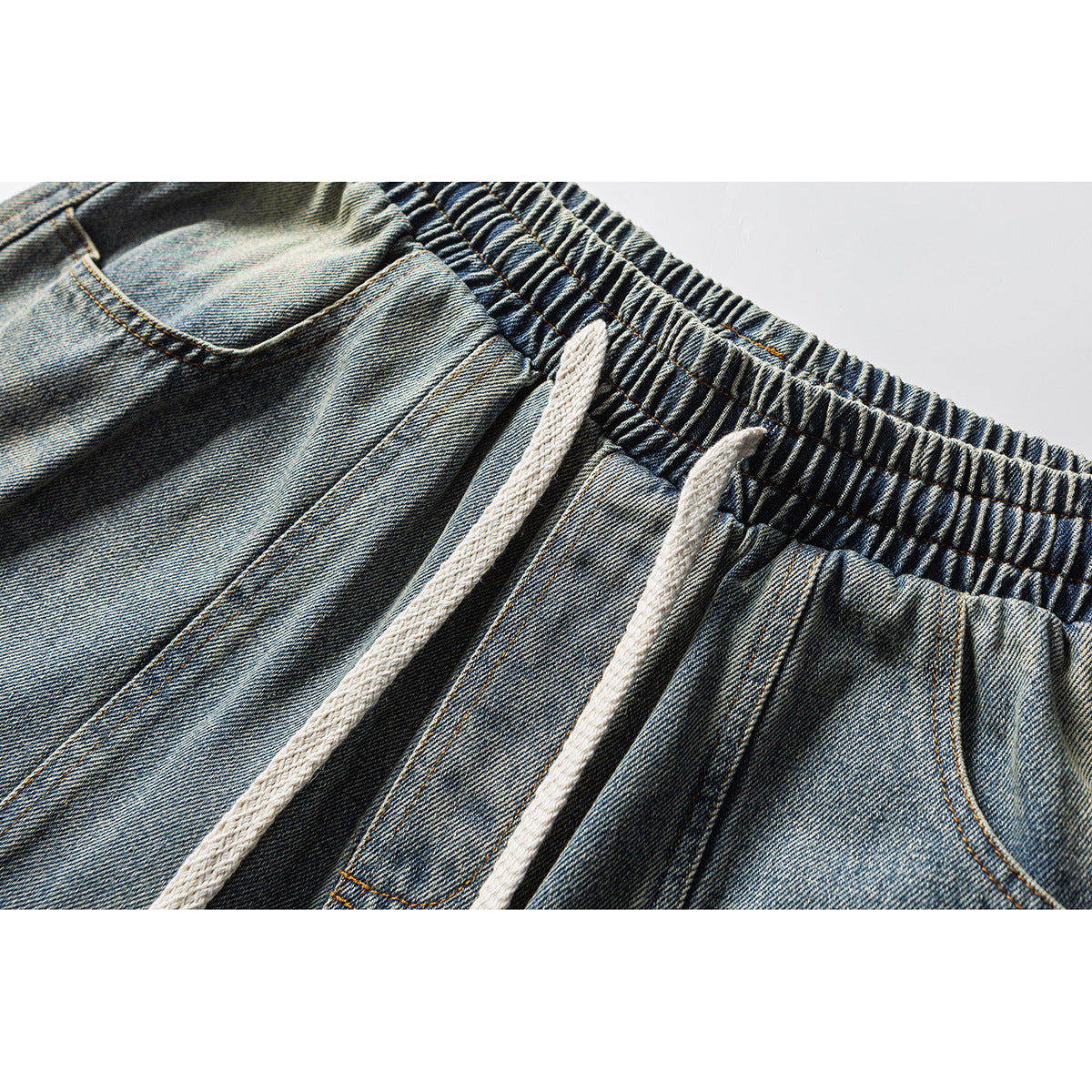 Close-up of blue denim shorts with an elastic waistband, white drawstrings and a front pocket.