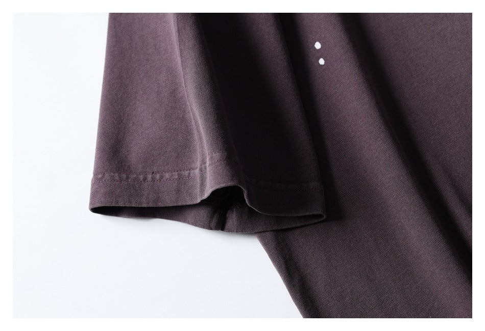 Close-up of a dark plum short-sleeve shirt showing the sleeve hem and two small white paint-like dots.