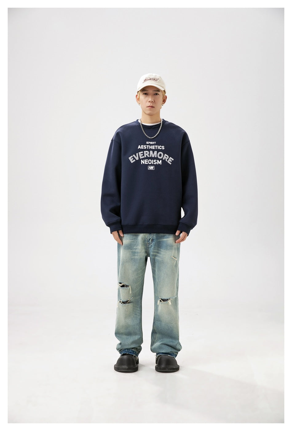 Front view of a model wearing a navy crewneck sweatshirt with white chest lettering and distressed light blue jeans.