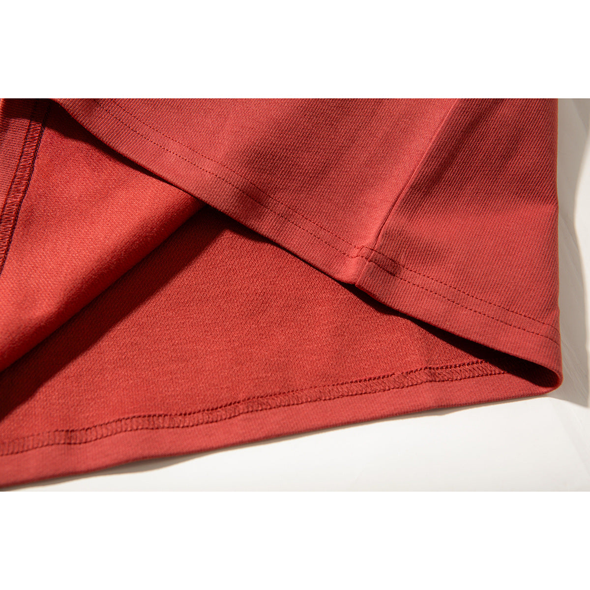 Close-up of the muted red T-shirt’s hem, showing the fabric and double-row stitching.
