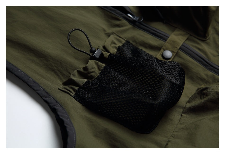 Close-up of an olive-green garment with a black mesh pocket, cord loop, snap, and dark trim.