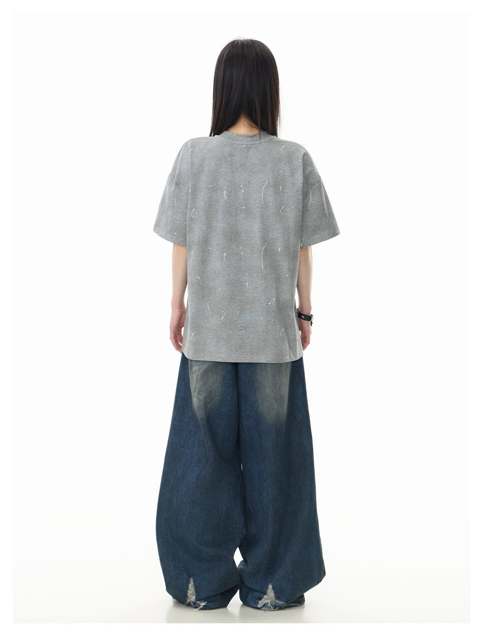Back view of a model wearing an oversized gray marked T-shirt and loose dark blue jeans.