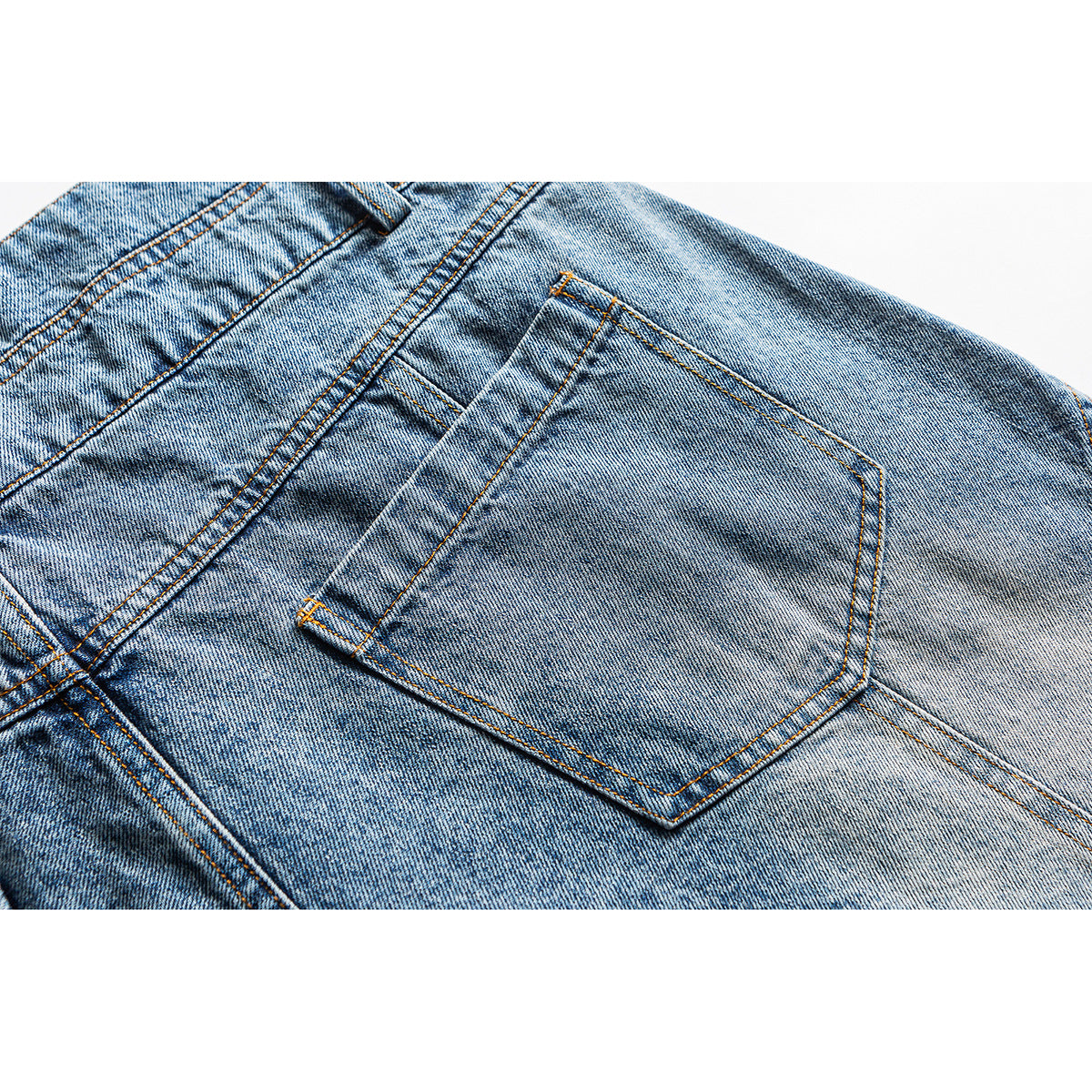 Close-up of a light blue denim back pocket with orange stitching and faded wash.