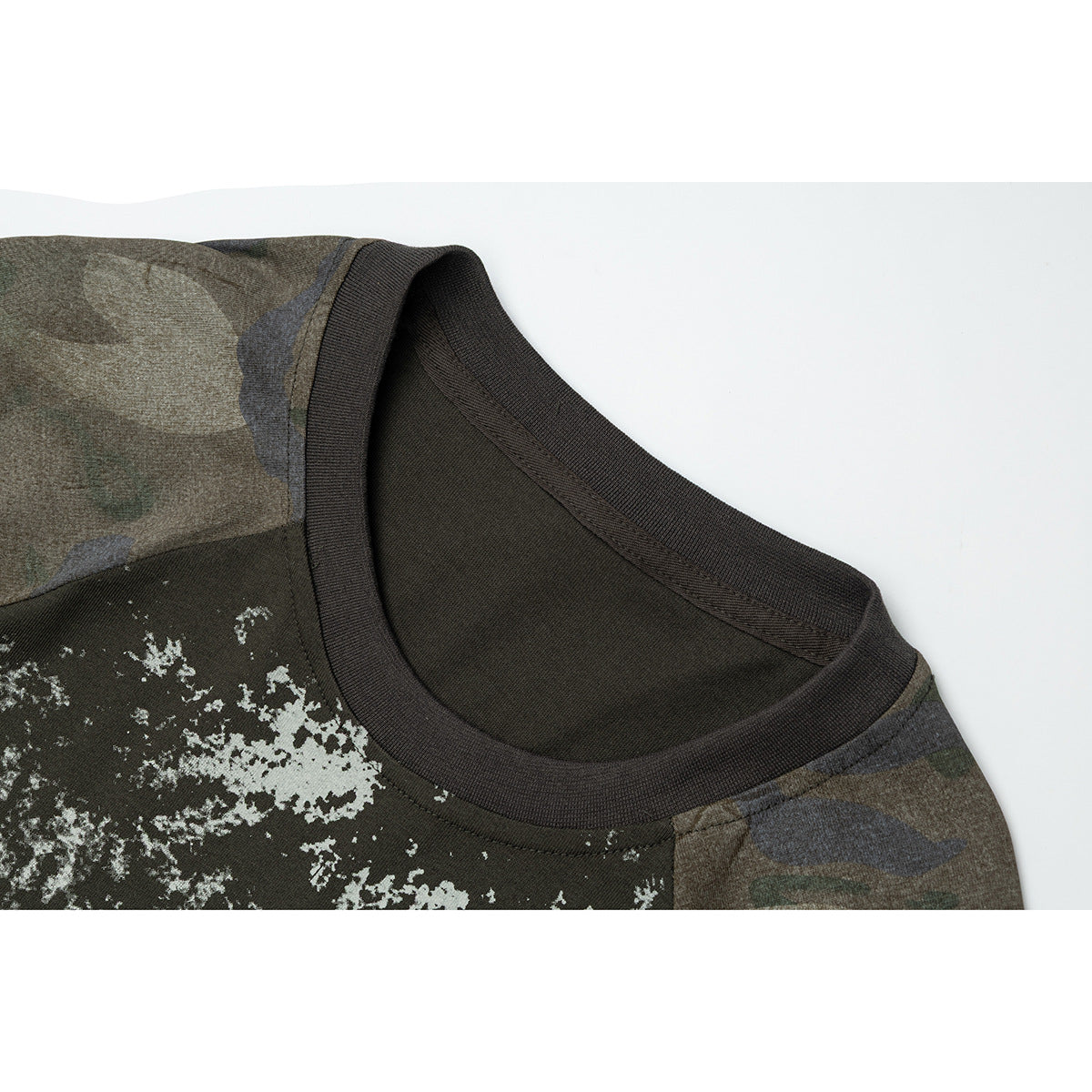 Close-up of a dark olive T-shirt neckline, distressed light graphic, and muted camouflage shoulder panel.