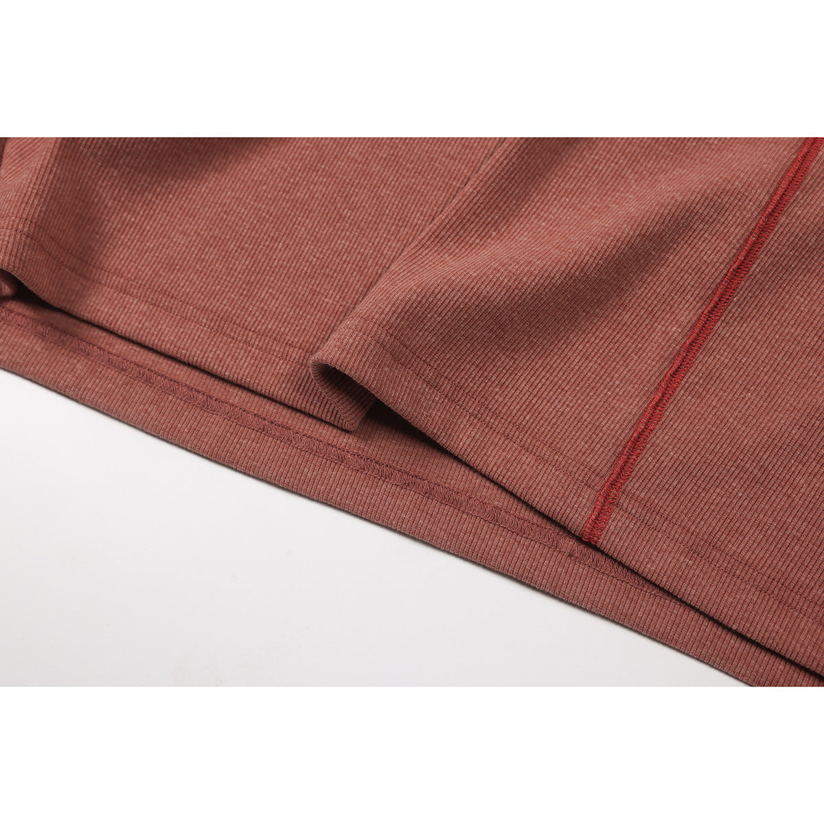 Close-up of the dusty rose ribbed top's sleeve edge, hem, and red seam stitching.