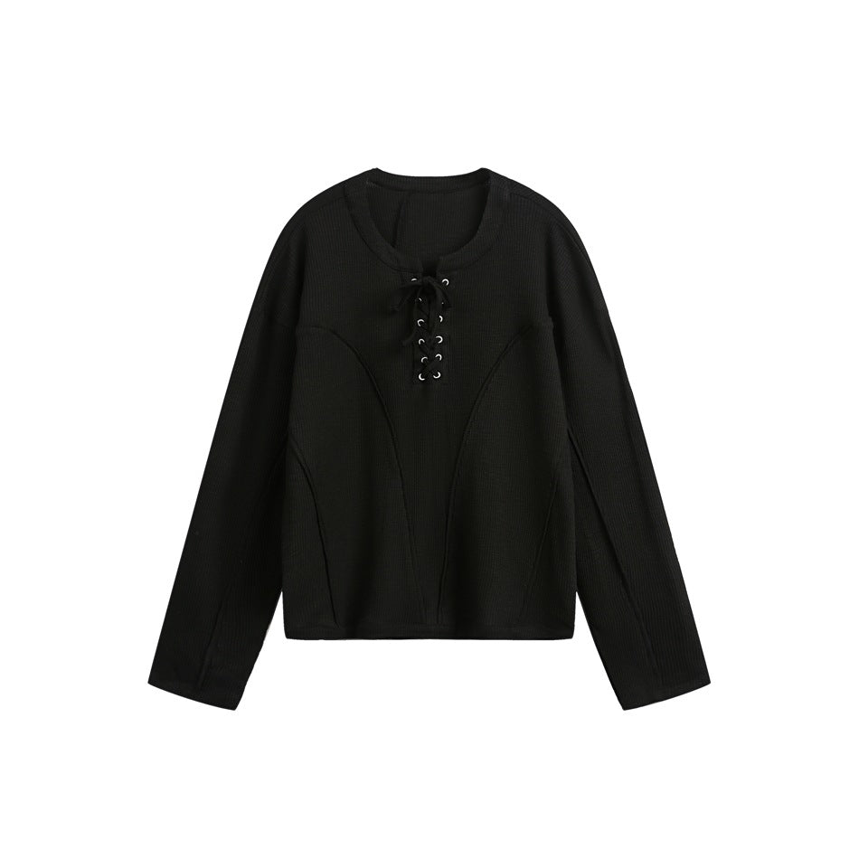 Black long-sleeve pullover with lace-up eyelet neckline and curved seam details, flat lay on white background