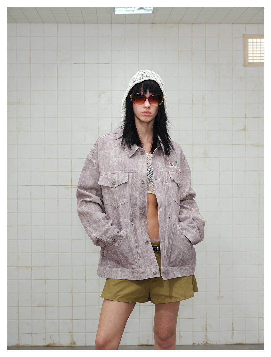 Model wearing an oversized dusty mauve jacket with flap pockets and floral chest embroidery, paired with olive shorts.
